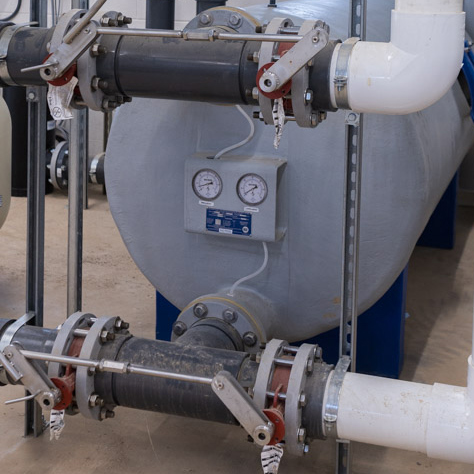 Pictured in this image is a grey,fiberglass pool filter with plumbing and face piping ttached. It is in service in a filter room at a water park.