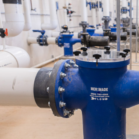 this image shows a water park filter room with piping and plumbing and pumps and blue mermade filter strainer basket housings.