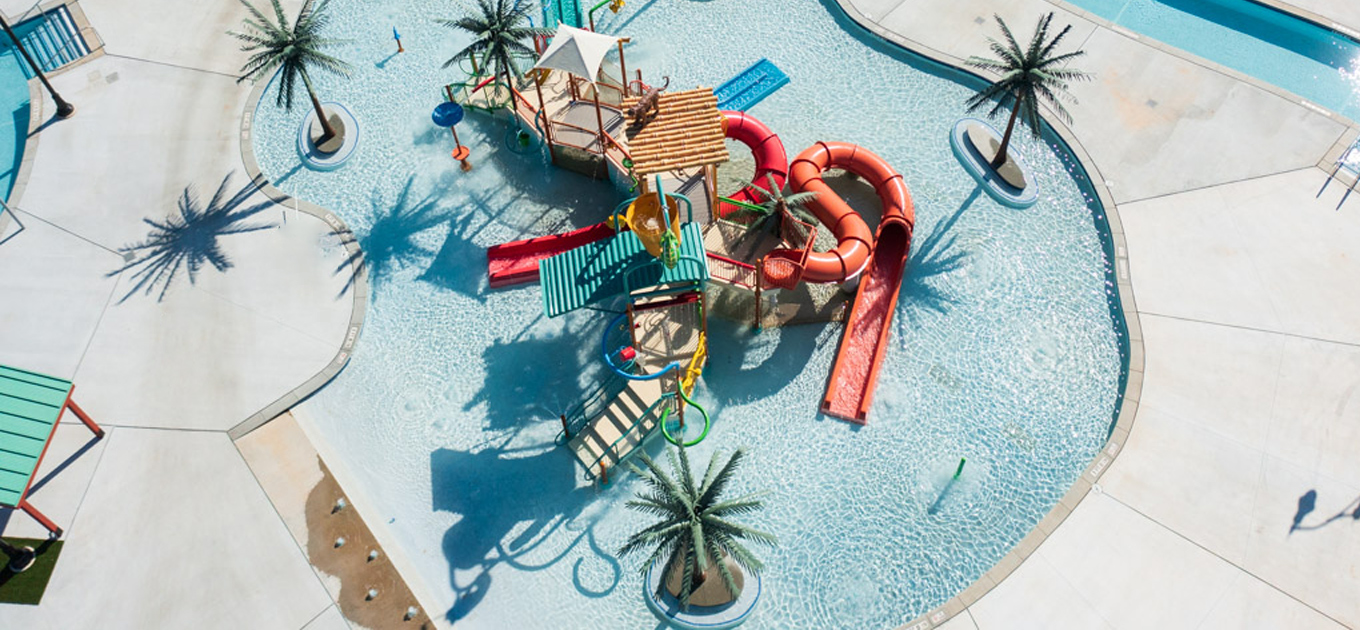 Images shows an aerial view of a new contruction kiddie-pool in a greater Atlanta area water park. The pool consists of 2 red water slides, palm trees, a bucket dump and playground.