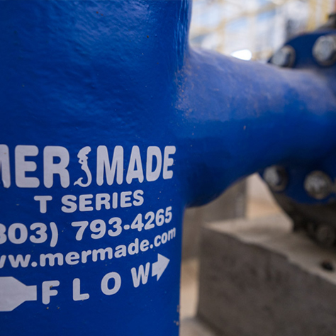 This image is a close up of a mermade filter t-series fiberglass strainer housing connected to a pump in a filter room.